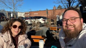 Ben Bond and Shelly Christensen smile while having coffee outside in a shopping center