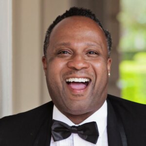 Lawon Exum smiling headshot wearing a black suit and black bow tie