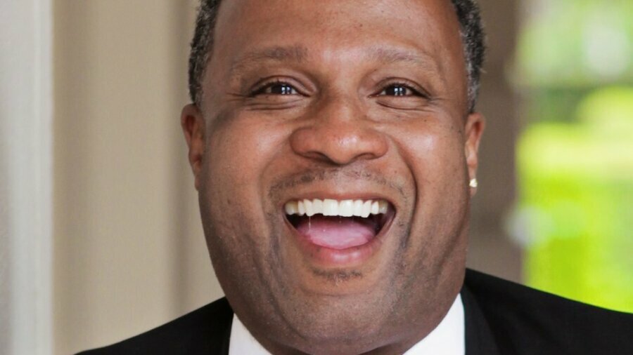 Lawon Exum smiling headshot wearing a black suit and black bow tie