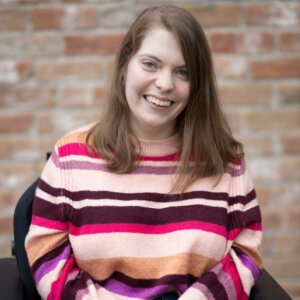 Nicole Zimmerer smiling headshot seated in front of a brick wall