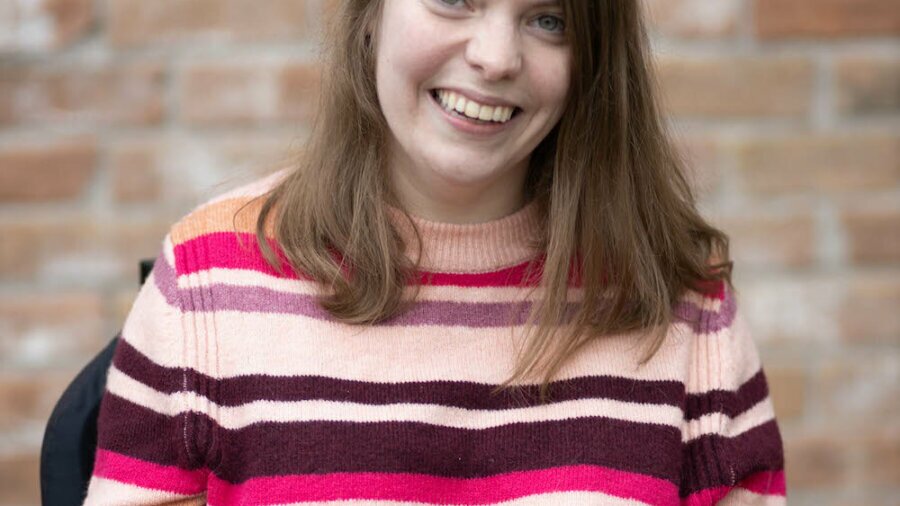 Nicole Zimmerer smiling headshot seated in front of a brick wall