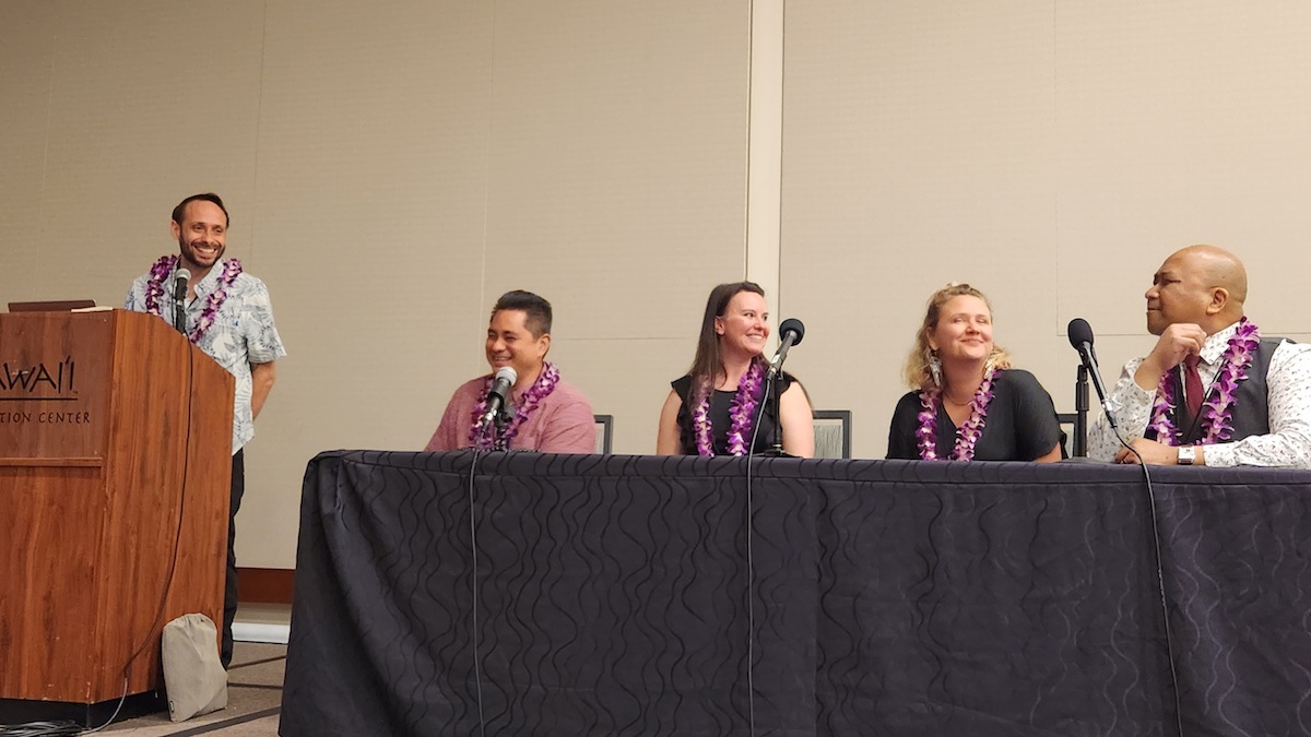 Wally Tablit speaking on a panel in Hawaii at a workforce development conference with three other panelists at the table and the moderator behind a podium