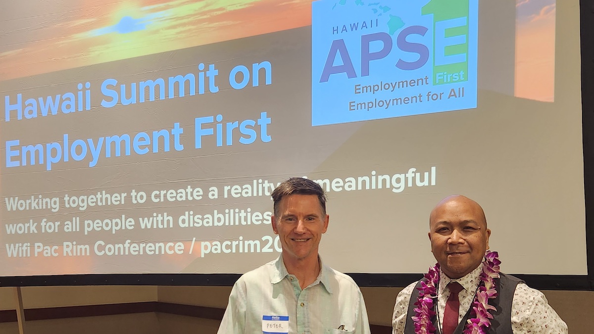 Wally and Peter Bernick smile together in front of a screen showing the APSE logo and text reading "Hawaii Summit on Employment First"