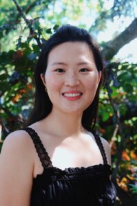 an Asian American woman smiling with greenery in the background