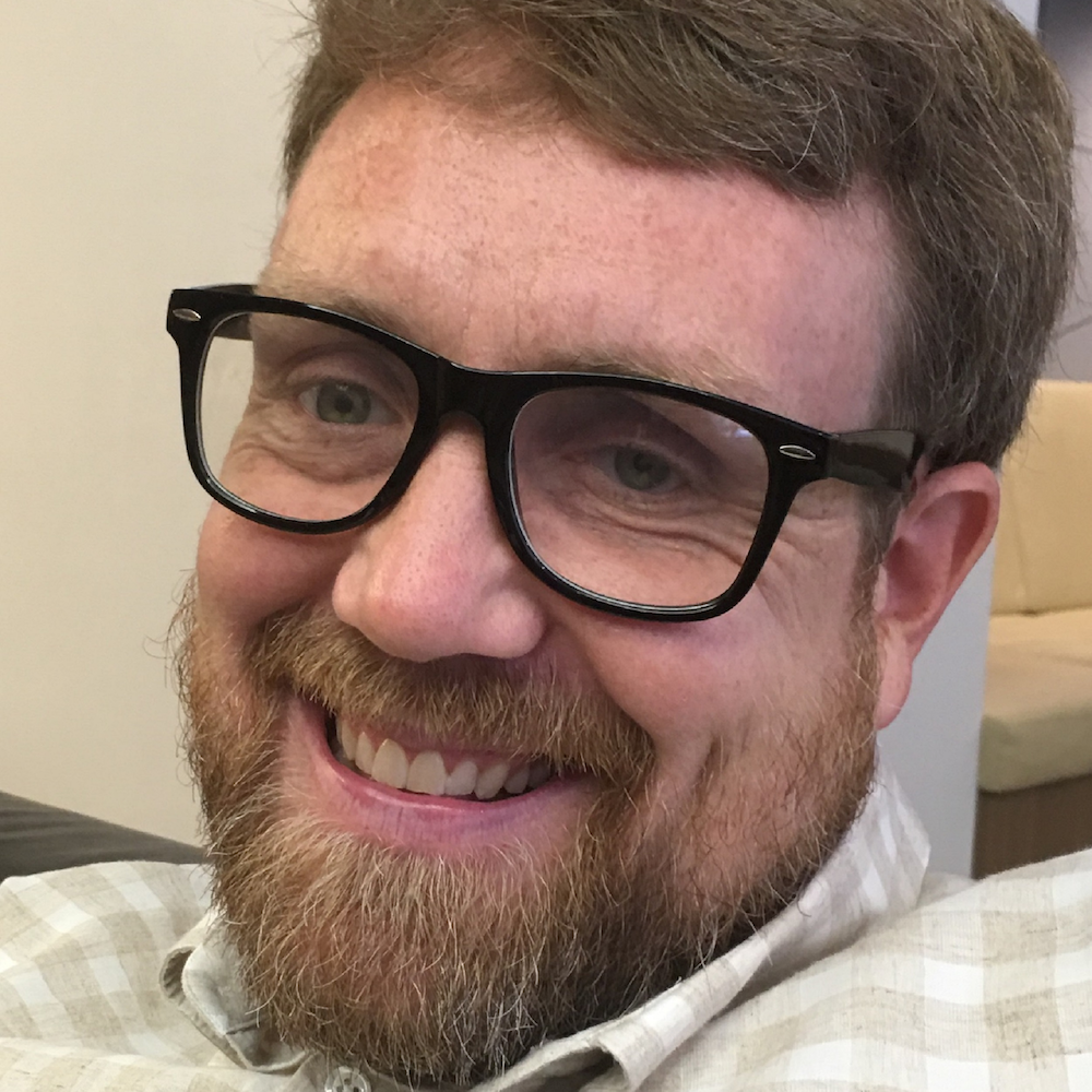 Adam Linn smiling headshot wearing glasses.