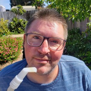 Brian Koukol smiling in a backyard with a tube next to his mouth