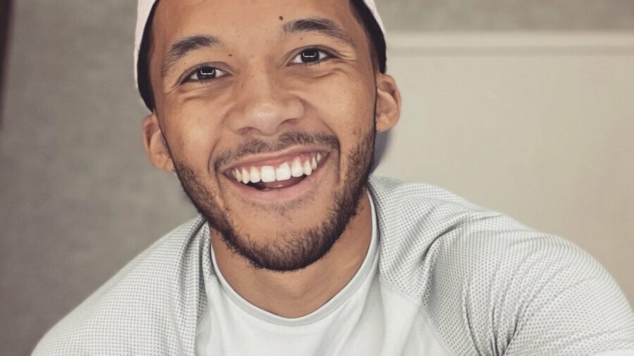 Isaiah Cane smiling headshot wearing a pink hat