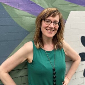 Shannon Rayne smiling in front of a painted brick wall