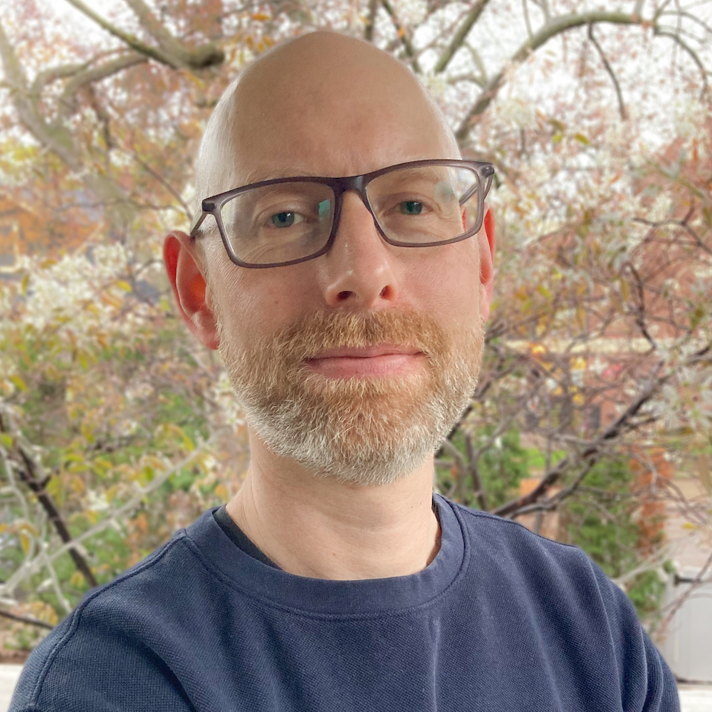 Trevor Finn smiling in front of trees wearing glasses