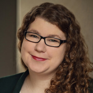 Hannah Roussel smiling headshot wearing a blazer and glasses