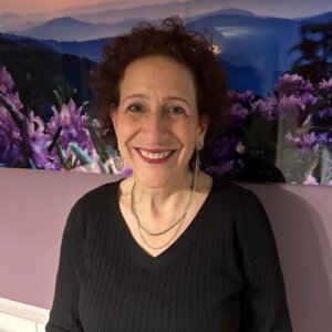 Karyn Harvey smiling in front of a mural of mountains and flowers.