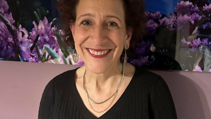 Karyn Harvey smiling in front of a mural of mountains and flowers.