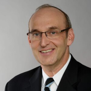 Howard Blas smiling headshot wearing glasses and a suit and tie