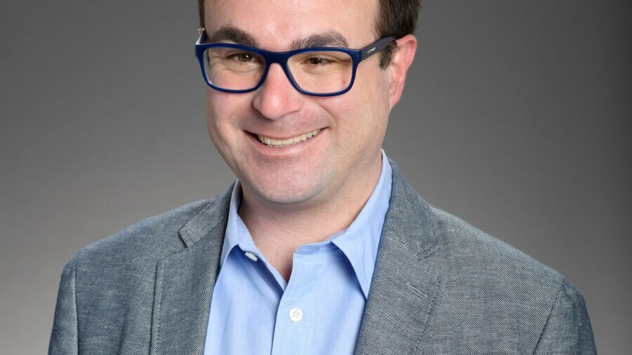 Nathan Varni smiling headshot wearing a blue shirt and grey blazer