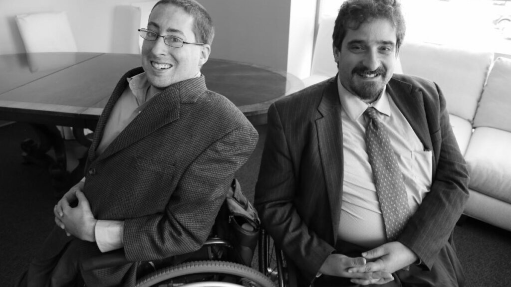 Greyscale photo of Ben Spangenberg and Justin Chappell smiling together wearing suits.