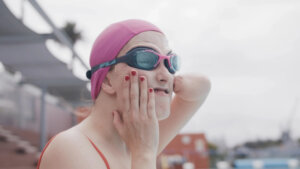 Still from "Inspire Me" with the director wearing a swimsuit, goggles, and swim cap, training for the paralympics