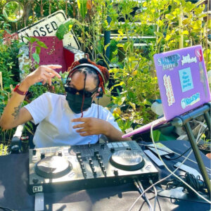Sabeerah Najee DJ'ing while wearing a face mask outside in front of trees and bushes