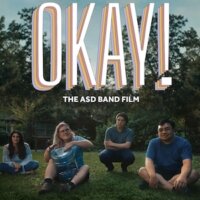 still from OKAY! with four of the subjects of the film sitting on grass outside