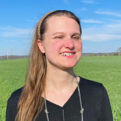 Hannah Harriman smiling headshot standing in front of a grass field