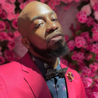 Steven McCoy headshot wearing a pink suit in front of pink flowers