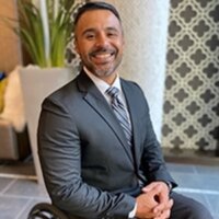 Angel Ponce smiling headshot wearing a suit and tie seated in his wheelchair