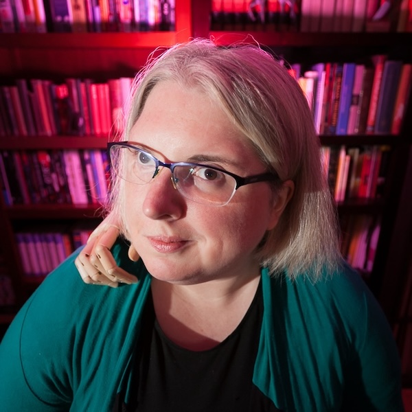 Ariel Baska smiling headshot in front of a bookshelf