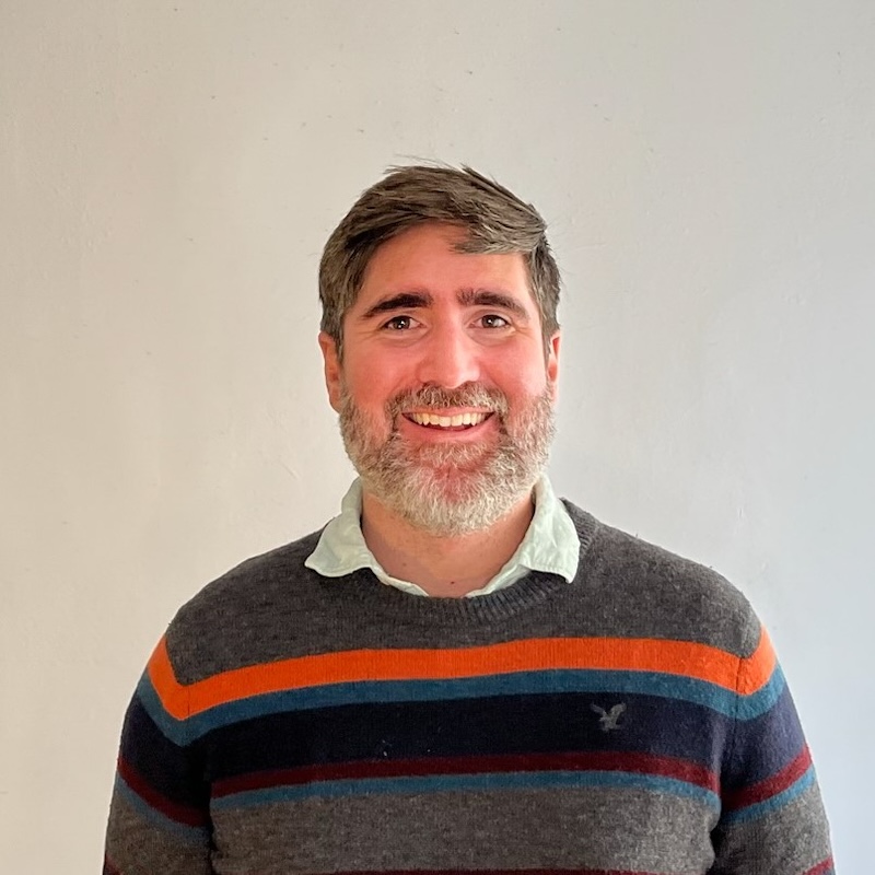 David Dineen-Porter smiling headshot wearing a gray sweater with colorful stripes
