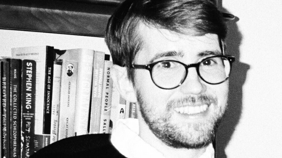 Johnny Bauers smiling headshot in black and white in front of a bookshelf