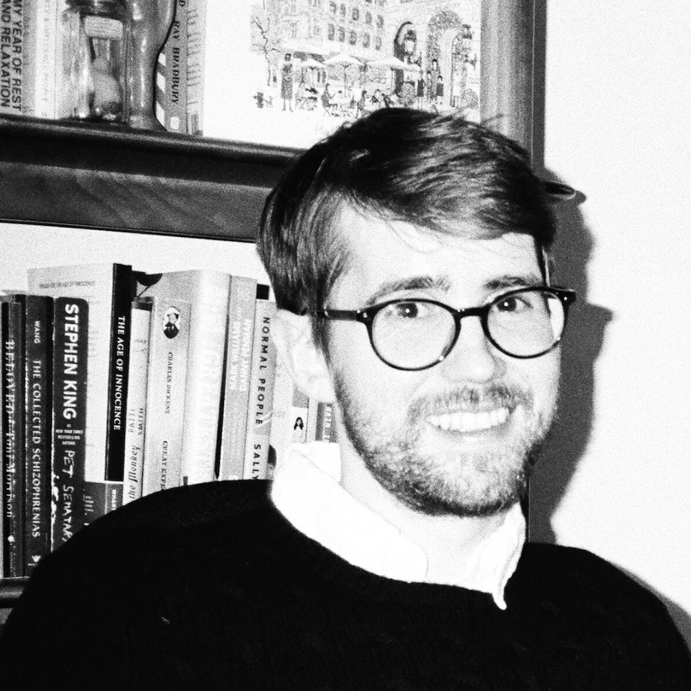 Johnny Bauers smiling headshot in black and white in front of a bookshelf