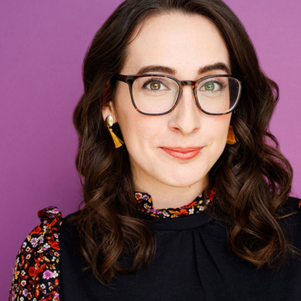 Liz Galalis smiling headshot wearing glasses and a flowery top