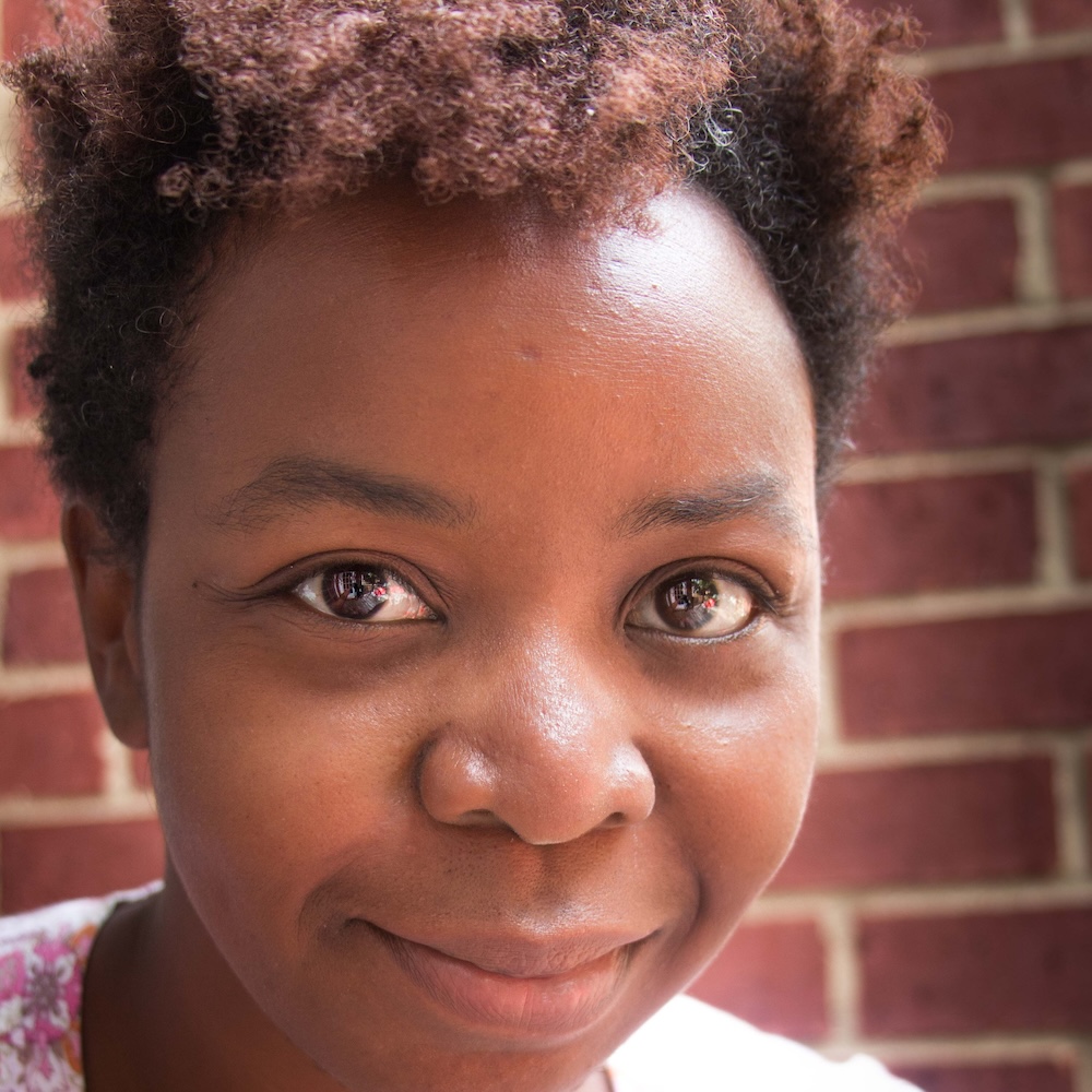 Sandrene Mathews smiling headshot in front of a brick wall
