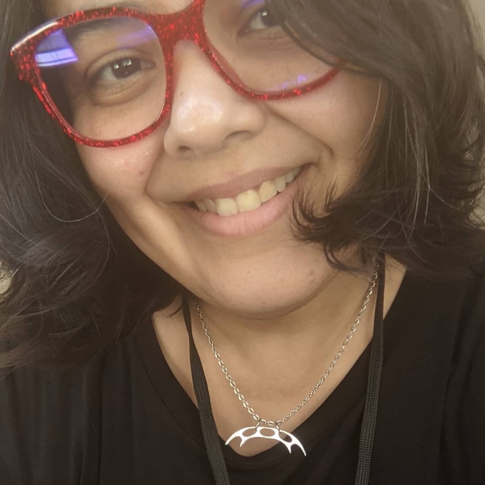 Teresa Jusino smiling headshot wearing red glasses