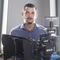 Toj Mora headshot standing behind a camera