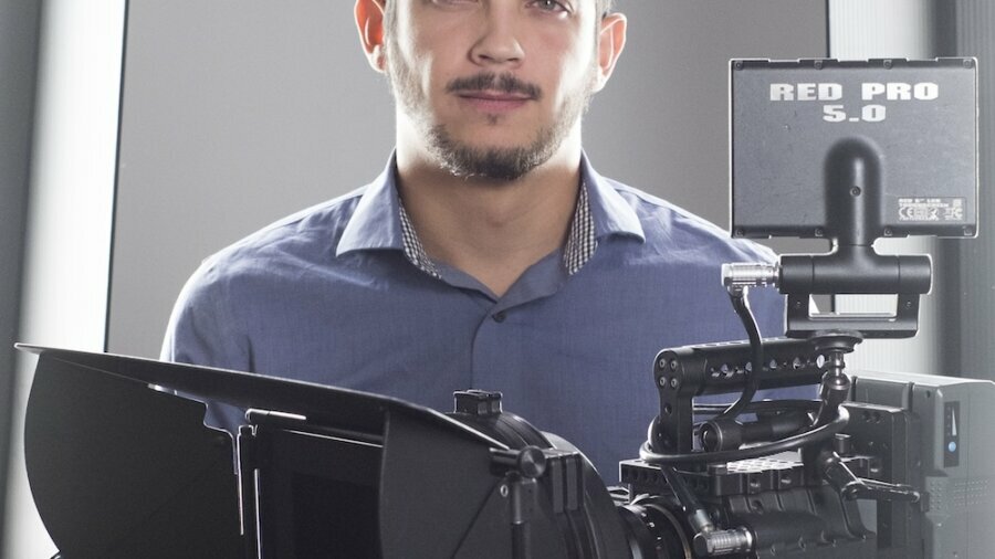 Toj Mora headshot standing behind a camera