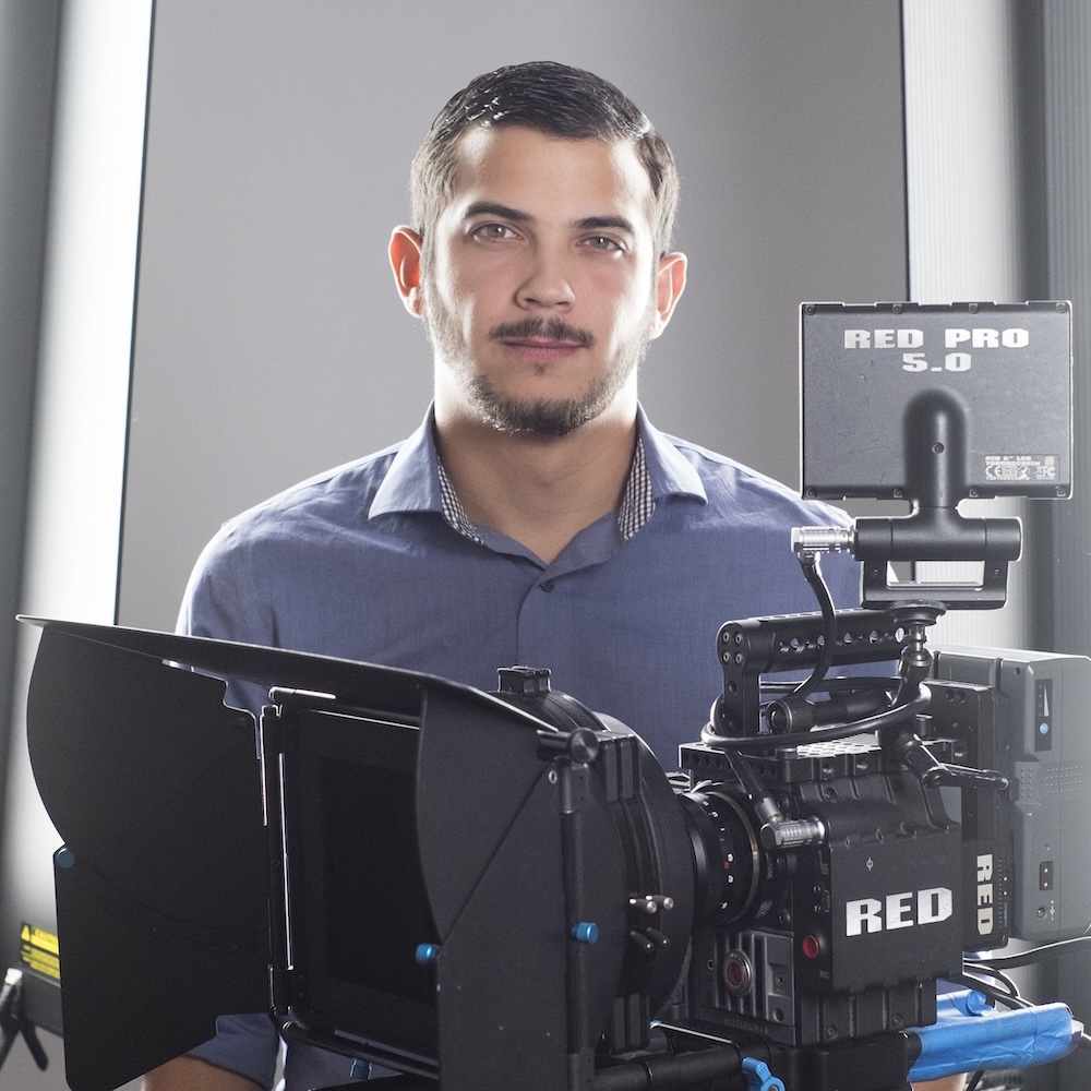 Toj Mora headshot standing behind a camera
