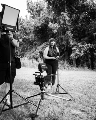 black and white photo of Maureen McEly smiling on the set of her short film Golden Hour with cameras and lighting equipment around her