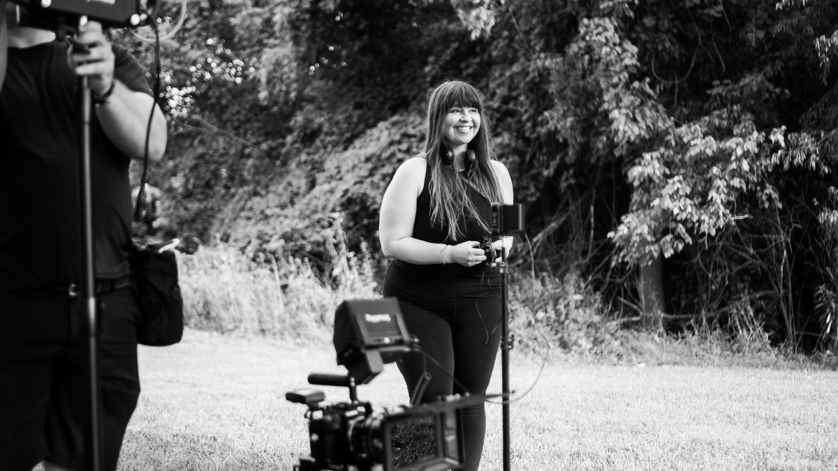 black and white photo of Maureen McEly smiling on the set of her short film Golden Hour with cameras and lighting equipment around her