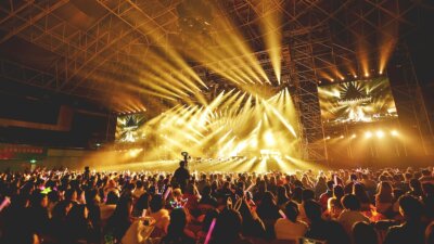 a packed arena during a concert with yellow and orange lighting on the stage
