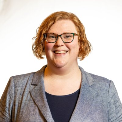 Ariel Simms smiling headshot wearing a grey blazer and a black shirt