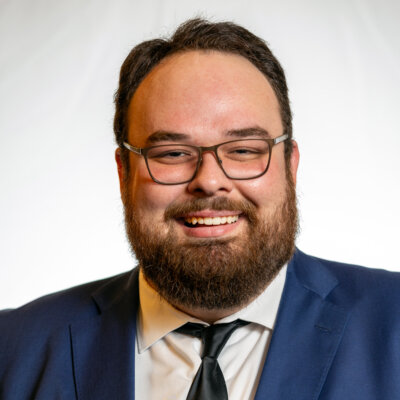 Ben Bond smiling headshot wearing a navy blue blazer, a white dress shirt, and a black tie