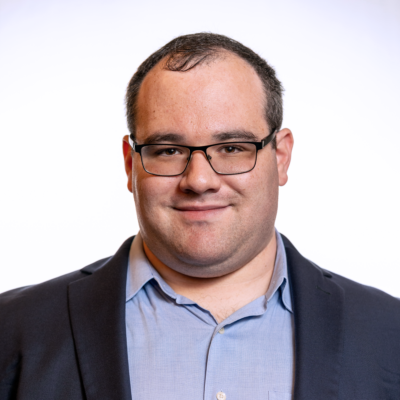 Eric Ascher smiling headshot wearing a dark blue blazer and a light blue dress shirt