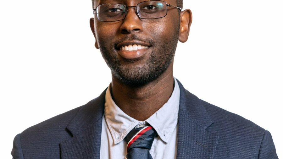 Ian Cherutich smiling headshot wearing a navy blue blazer, a dress shirt, and a red white and blue tie