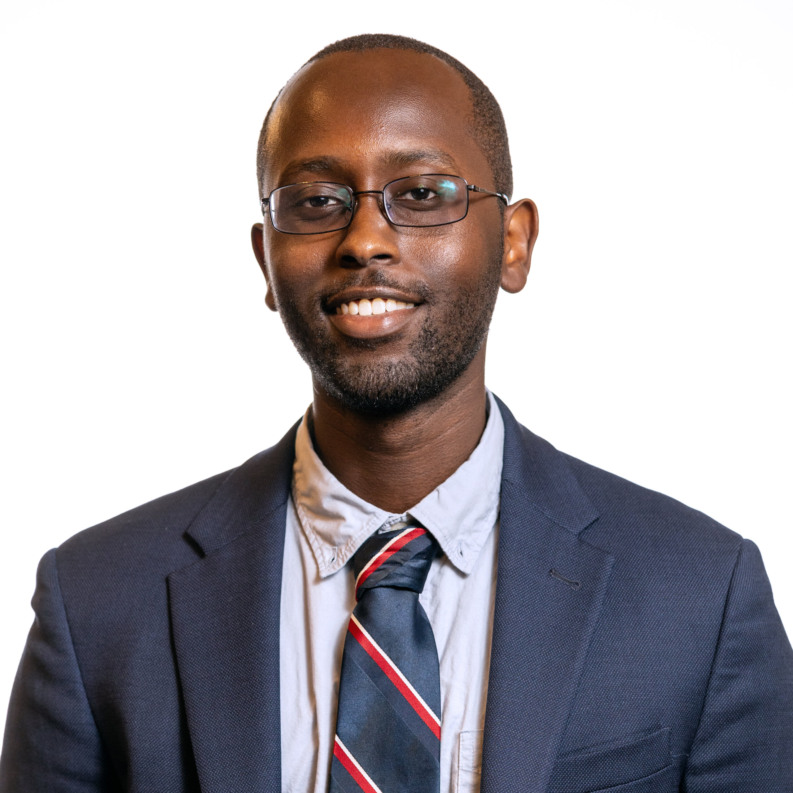 Ian Cherutich smiling headshot wearing a navy blue blazer, a dress shirt, and a red white and blue tie