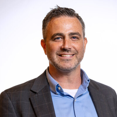 Kevin McCloskey smiling headshot wearing a grey blazer and blue dress shirt