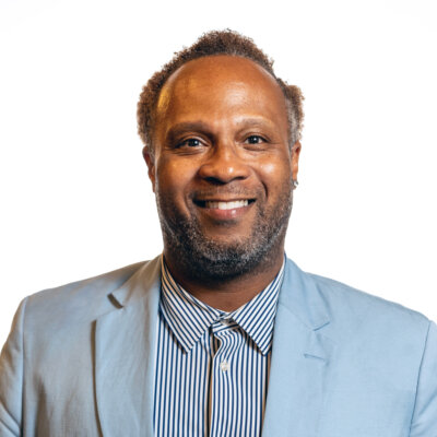 Lawon Exum smiling headshot wearing a light blue blazer and striped dress shirt
