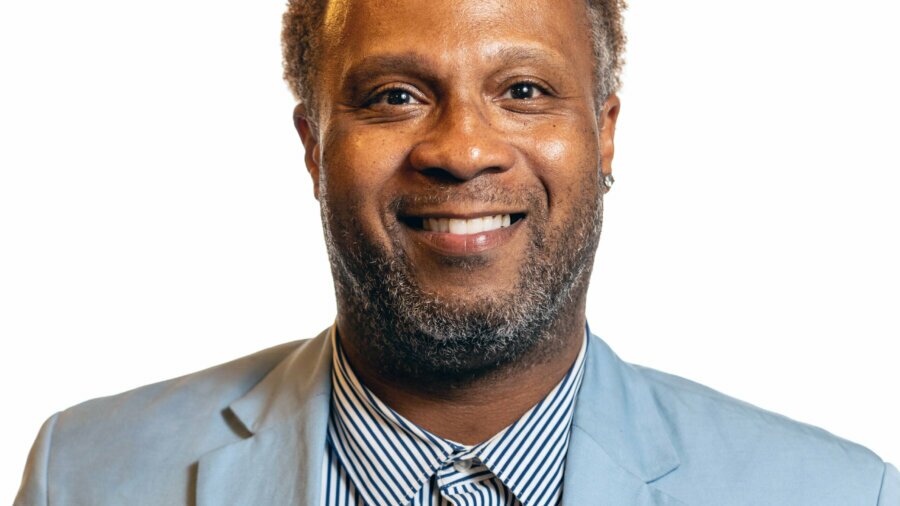 Lawon Exum smiling headshot wearing a light blue blazer and striped dress shirt