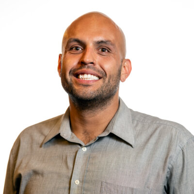 Phillip Saldana smiling headshot wearing a bluish-grey dress shirt