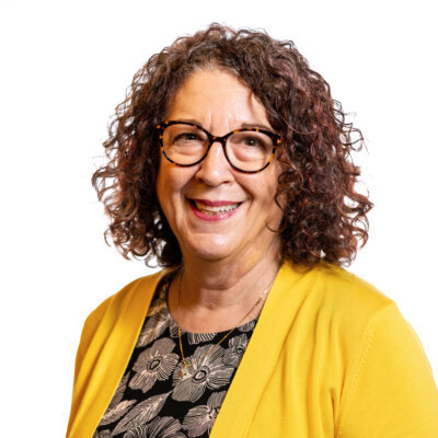 Shelly Christensen smiling headshot wearing a yellow jacket and a flowery shirt