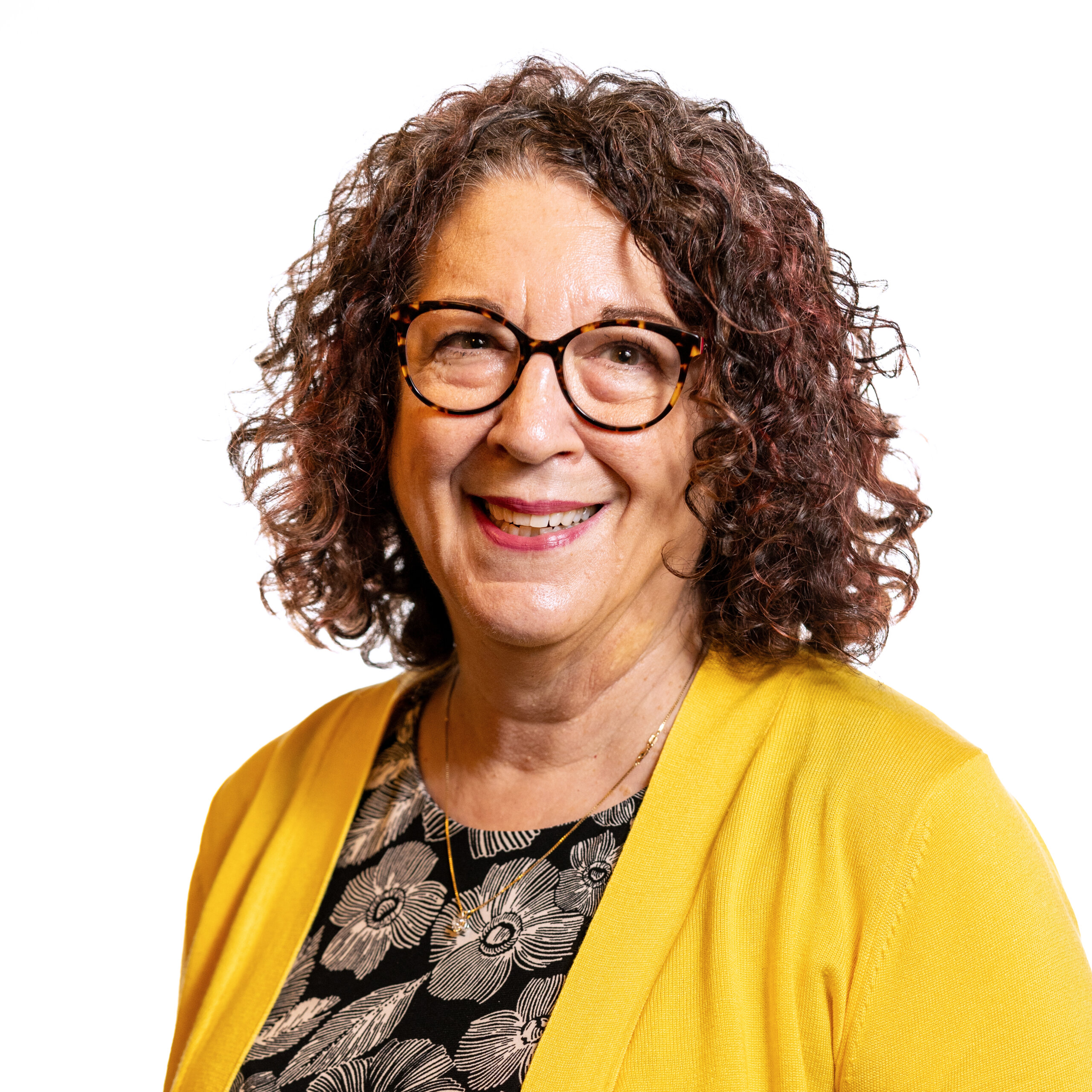 Shelly Christensen smiling headshot wearing a yellow jacket and a flowery shirt