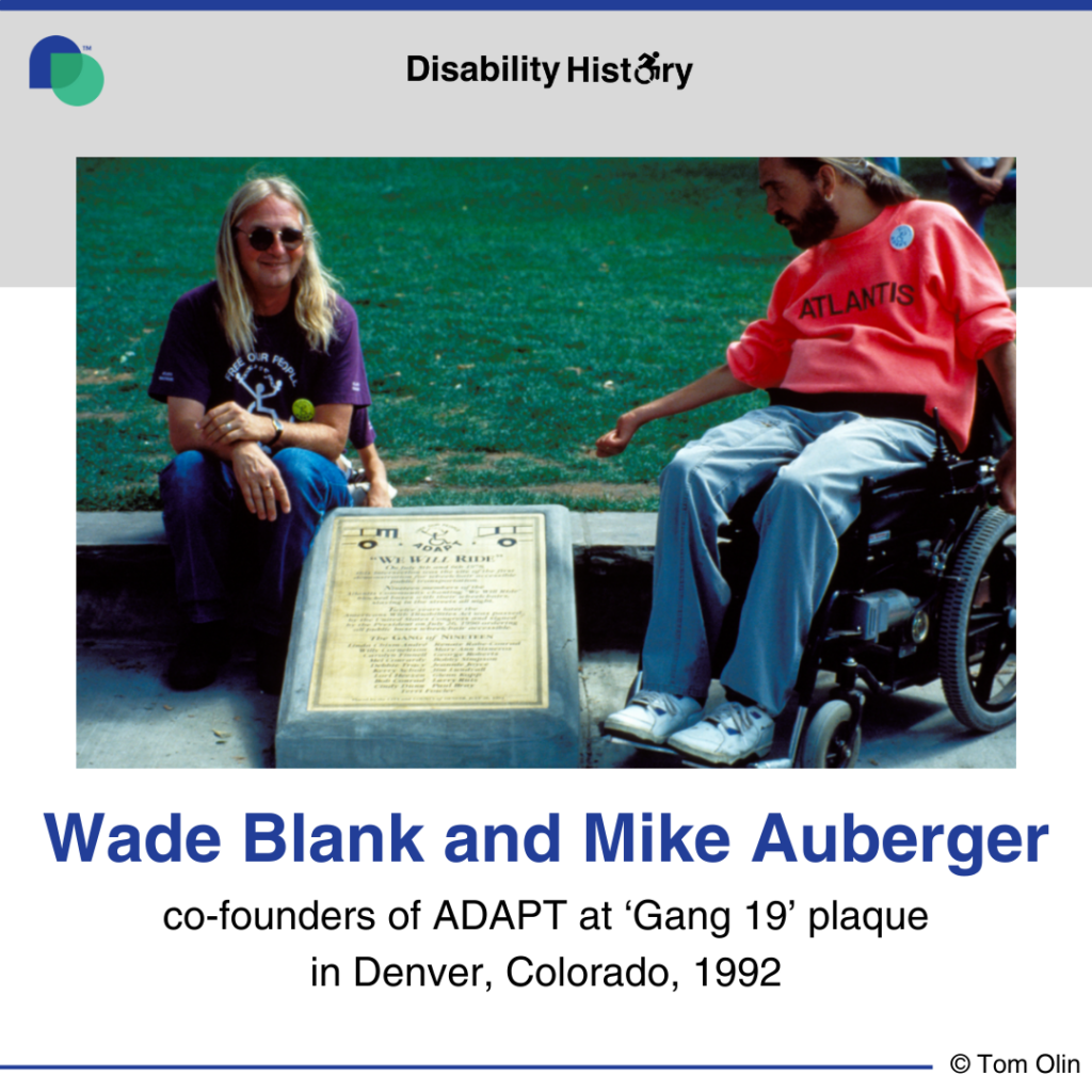 photo of Wade Blank and Mike Auberger next to Gang of 19 plaque on the side walk with ADAPT logo and ‘We will ride” visible. Text: Wade Blank and Mike Auberger. co-founders of ADAPT at 'Gang of 19' plaque. Denver, Colorado. 1992. Source: Tom Olin